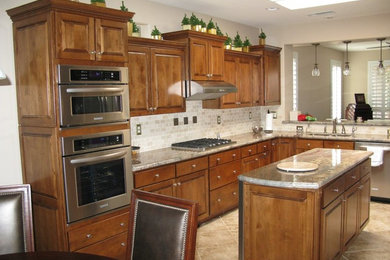 Inspiration for a large transitional l-shaped porcelain tile eat-in kitchen remodel in Phoenix with an undermount sink, raised-panel cabinets, medium tone wood cabinets, quartz countertops, beige backsplash, stone tile backsplash, stainless steel appliances and an island