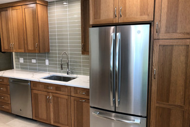 This is an example of a small transitional galley kitchen in Chicago with a single-bowl sink, flat-panel cabinets, medium wood cabinets, quartz benchtops, green splashback, glass tile splashback, stainless steel appliances, no island, grey floor and multi-coloured benchtop.