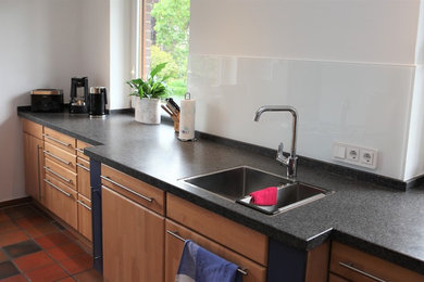 ハンブルクにある広いコンテンポラリースタイルのおしゃれなキッチン (ドロップインシンク、御影石カウンター、白いキッチンパネル、ガラス板のキッチンパネル) の写真