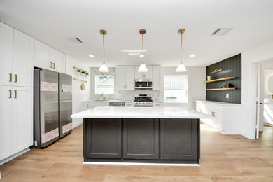 Mid-sized farmhouse l-shaped vinyl floor and beige floor open concept kitchen photo in Houston with a double-bowl sink, shaker cabinets, black cabinets, quartz countertops, white backsplash, quartz backsplash, stainless steel appliances, an island and white countertops
