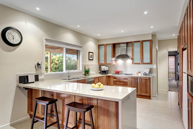 Design ideas for a large contemporary u-shaped kitchen in Melbourne with a drop-in sink, glass-front cabinets, dark wood cabinets, limestone benchtops, white splashback, ceramic splashback, stainless steel appliances, ceramic floors, no island, white floor and white benchtop.