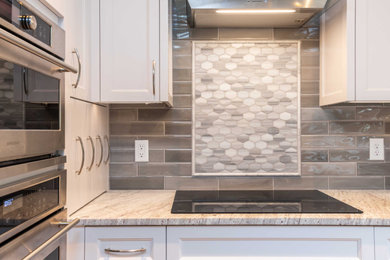 This is an example of a mid-sized transitional u-shaped kitchen in Minneapolis with a single-bowl sink, shaker cabinets, white cabinets, granite benchtops, grey splashback, subway tile splashback, stainless steel appliances, medium hardwood floors, no island, brown floor and white benchtop.