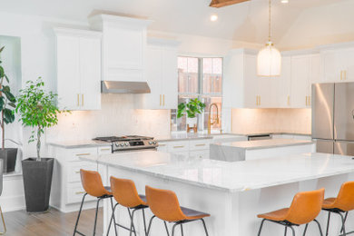 Inspiration for a large transitional porcelain tile and beige floor kitchen remodel in Dallas with a farmhouse sink, shaker cabinets, white cabinets, quartzite countertops, white backsplash, ceramic backsplash, stainless steel appliances, two islands and gray countertops