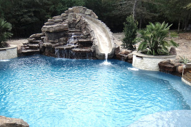 Aménagement d'une grande piscine arrière exotique sur mesure avec un toboggan.