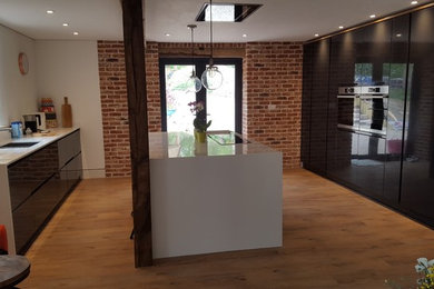Photo of a large contemporary u-shaped open plan kitchen in Cambridgeshire with a double-bowl sink, flat-panel cabinets, white cabinets, quartz worktops, white splashback, stainless steel appliances, vinyl flooring, an island and beige floors.