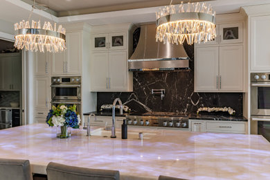 Example of a large trendy l-shaped vinyl floor and brown floor open concept kitchen design in Milwaukee with an undermount sink, recessed-panel cabinets, white cabinets, quartzite countertops, black backsplash, stone slab backsplash, stainless steel appliances, an island and beige countertops