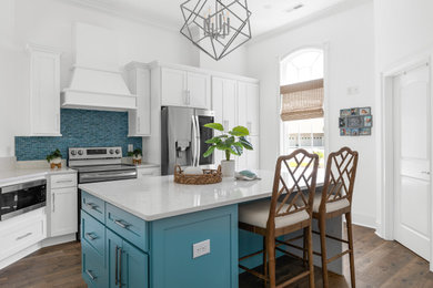 Example of a large beach style l-shaped vinyl floor, brown floor and vaulted ceiling enclosed kitchen design in Charleston with a farmhouse sink, raised-panel cabinets, white cabinets, quartz countertops, blue backsplash, mosaic tile backsplash, stainless steel appliances, an island and white countertops
