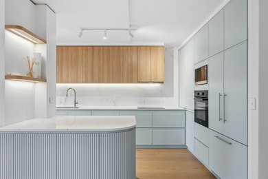 Inspiration for a mid-sized beach style u-shaped open plan kitchen in Sydney with with island, an undermount sink, shaker cabinets, green cabinets, granite benchtops, granite splashback, black appliances, laminate floors, brown floor and white benchtop.