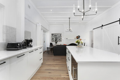 This is an example of a modern galley open plan kitchen in Sydney with white cabinets, quartz benchtops, grey splashback, stone slab splashback, stainless steel appliances, light hardwood floors, with island and white benchtop.