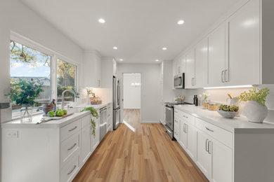 Open concept kitchen - large galley vinyl floor and brown floor open concept kitchen idea in San Francisco with an undermount sink, shaker cabinets, white cabinets, quartz countertops, white backsplash, quartz backsplash, stainless steel appliances, no island and white countertops