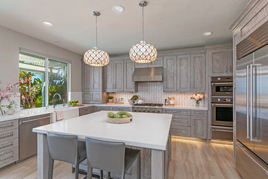 Large transitional kitchen in San Diego with a farmhouse sink, recessed-panel cabinets, grey cabinets, quartz benchtops, grey splashback, marble splashback, stainless steel appliances, porcelain floors, with island, grey floor and white benchtop.