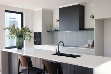 This is an example of a mid-sized modern galley open plan kitchen in Canberra - Queanbeyan with an undermount sink, grey cabinets, quartz benchtops, grey splashback, mosaic tile splashback, black appliances, vinyl floors, with island, brown floor and white benchtop.