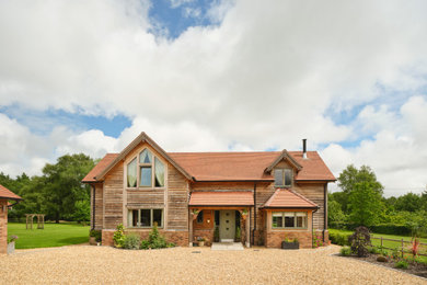 Photo of a mid-sized two-storey house exterior in Hampshire with wood siding, a gable roof, a tile roof, a red roof and board and batten siding.