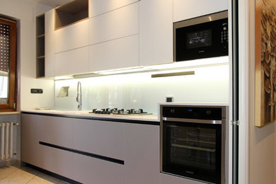 Immagine di una cucina parallela contemporanea chiusa e di medie dimensioni con lavello da incasso, ante di vetro, top in quarzo composito, paraspruzzi bianco, paraspruzzi con lastra di vetro, elettrodomestici in acciaio inossidabile e nessuna isola