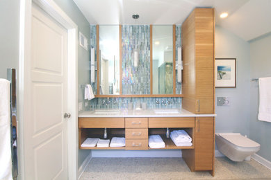 Corner shower - mid-sized modern master multicolored tile and glass sheet porcelain tile and gray floor corner shower idea in Wiltshire with flat-panel cabinets, light wood cabinets, gray walls, quartz countertops, a wall-mount toilet, an undermount sink and a hinged shower door