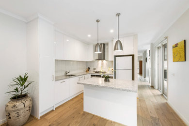 This is an example of a small modern l-shaped eat-in kitchen in Melbourne with a drop-in sink, flat-panel cabinets, white cabinets, limestone benchtops, grey splashback, ceramic splashback, stainless steel appliances, light hardwood floors, with island, beige floor and grey benchtop.