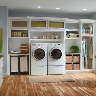 Imagen de lavadero multiusos y en L, clásico, grande, con armarios tipo vitrina, puertas de armario blancas, lavadora y secadora juntas, suelo de madera en tonos medios y paredes grises