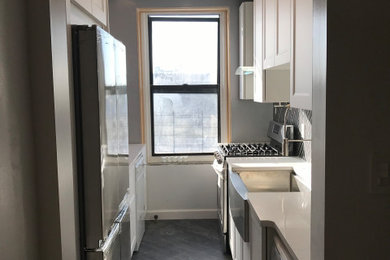 Example of a small minimalist galley vinyl floor and green floor enclosed kitchen design in New York with a farmhouse sink, shaker cabinets, white cabinets, quartzite countertops, black backsplash, ceramic backsplash, stainless steel appliances, no island and white countertops