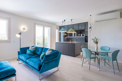 This is an example of a medium sized modern l-shaped open plan kitchen in Rome with a submerged sink, glass-front cabinets, turquoise cabinets, composite countertops, black splashback, light hardwood flooring, an island, beige floors and black worktops.