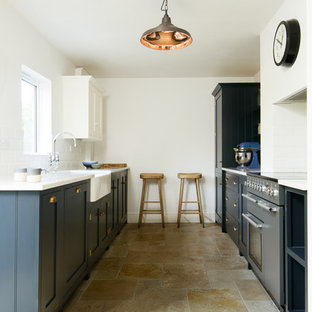 Удачное сочетание для дизайна помещения: маленькая отдельная, параллельная кухня в стиле рустика с раковиной в стиле кантри, фасадами в стиле шейкер, синими фасадами, столешницей из акрилового камня, белым фартуком, фартуком из плитки кабанчик, черной техникой и полом из травертина без острова - самое интересное для вас