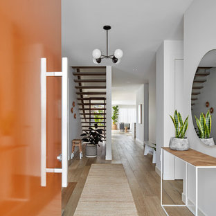 Immagine di un corridoio design con pareti bianche, una porta singola, una porta arancione, pavimento marrone e parquet chiaro