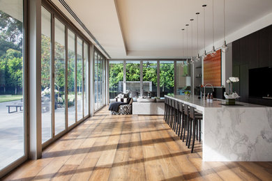 Large contemporary single-wall open plan kitchen in Melbourne with recessed-panel cabinets, dark wood cabinets, marble benchtops, with island, panelled appliances, a double-bowl sink, medium hardwood floors and brown floor.