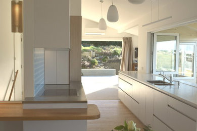 This is an example of a mid-sized scandinavian galley open plan kitchen in Christchurch with an undermount sink, flat-panel cabinets, white cabinets, solid surface benchtops, multi-coloured splashback, glass sheet splashback, stainless steel appliances, medium hardwood floors, no island and brown floor.