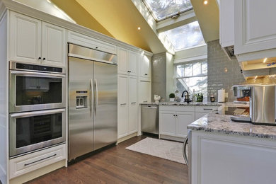 Inspiration for a large contemporary u-shaped light wood floor and brown floor open concept kitchen remodel in Calgary with white cabinets, granite countertops, an undermount sink, raised-panel cabinets, gray backsplash, subway tile backsplash, stainless steel appliances and an island