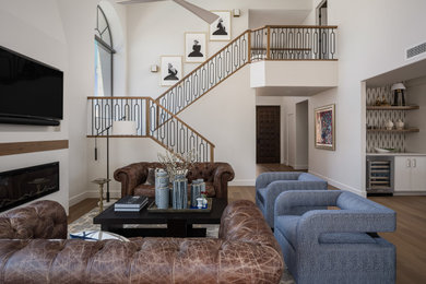 Inspiration for a mid-sized transitional open concept light wood floor, brown floor and wallpaper living room remodel in Phoenix with a bar, white walls, a standard fireplace, a plaster fireplace and a wall-mounted tv