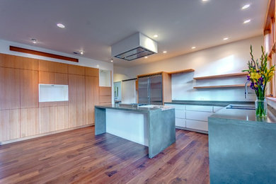 Inspiration for a mid-sized modern l-shaped open plan kitchen in Portland with an undermount sink, flat-panel cabinets, white cabinets, concrete benchtops, stainless steel appliances, medium hardwood floors and with island.