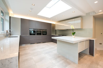 This is an example of a large contemporary u-shaped kitchen in London with an undermount sink, flat-panel cabinets, beige cabinets, marble benchtops, beige splashback, glass sheet splashback, black appliances and a peninsula.