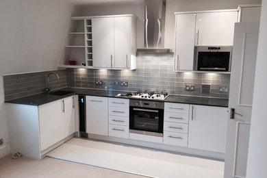 This is an example of a small modern l-shaped open plan kitchen in London with a built-in sink, flat-panel cabinets, white cabinets, granite worktops, metallic splashback, glass tiled splashback, white appliances, ceramic flooring, no island and grey floors.