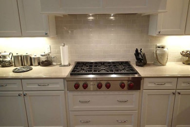 Mid-sized l-shaped medium tone wood floor open concept kitchen photo in Tampa with a farmhouse sink, shaker cabinets, white cabinets, white backsplash, subway tile backsplash, stainless steel appliances and an island