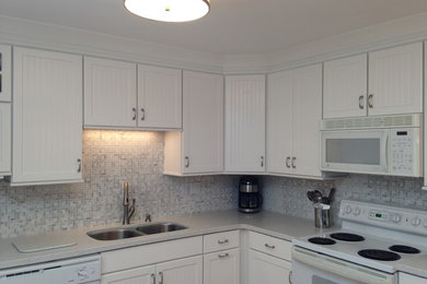 Mid-sized beach style l-shaped eat-in kitchen photo in Other with an undermount sink, beaded inset cabinets, white cabinets, solid surface countertops, gray backsplash, mosaic tile backsplash, white appliances and a peninsula