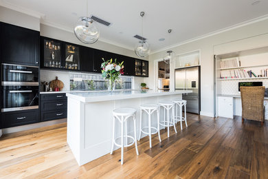 Inspiration for a transitional kitchen in Melbourne with shaker cabinets, black cabinets, window splashback, stainless steel appliances, medium hardwood floors, with island, brown floor and white benchtop.