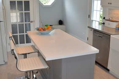 Example of a mid-sized transitional l-shaped vinyl floor and beige floor eat-in kitchen design in Toronto with a farmhouse sink, shaker cabinets, white cabinets, quartz countertops, gray backsplash, stainless steel appliances, an island and stone tile backsplash