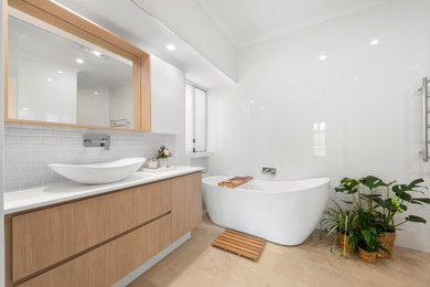 Tropical master wet room bathroom in Perth with shaker cabinets, light wood cabinets, a freestanding tub, a one-piece toilet, white tile, white walls, a vessel sink, brown floor, an open shower and white benchtops.
