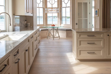 Example of a mid-sized beach style galley light wood floor and vaulted ceiling eat-in kitchen design in New York with an undermount sink, recessed-panel cabinets, white cabinets, granite countertops, white backsplash, granite backsplash, paneled appliances, an island and white countertops