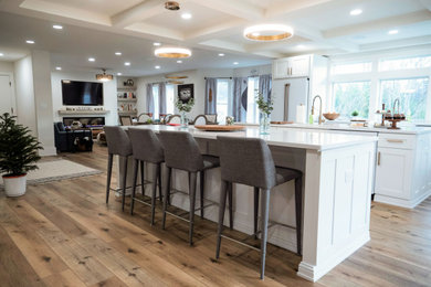 Example of a huge minimalist laminate floor, brown floor and coffered ceiling open concept kitchen design in Philadelphia with a farmhouse sink, shaker cabinets, white cabinets, wood countertops, white backsplash, quartz backsplash, white appliances, two islands and white countertops