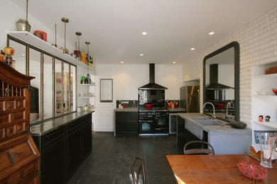 Inspiration pour une grande cuisine urbaine en U fermée avec un évier 2 bacs, un placard à porte affleurante, des portes de placard noires, un plan de travail en béton, une crédence noire, une crédence en ardoise, un électroménager noir, un sol en ardoise, 2 îlots, un sol noir et un plan de travail gris.