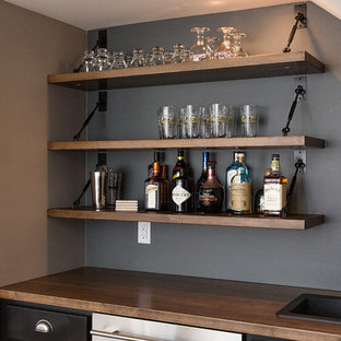 他の地域の大きいおしゃれなウェットバー (ドロップインシンク、落し込みパネル扉のキャビネット、木材カウンター、グレーのキッチンパネル、茶色いキッチンカウンター) の写真