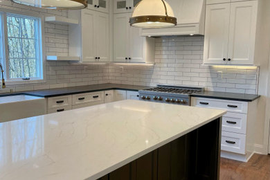 Example of a transitional dark wood floor eat-in kitchen design in New York with a farmhouse sink, recessed-panel cabinets, quartz countertops, white backsplash, subway tile backsplash, stainless steel appliances, an island and white countertops