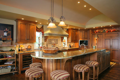 Inspiration for a large timeless l-shaped dark wood floor and brown floor eat-in kitchen remodel in Kansas City with medium tone wood cabinets, beige backsplash, an island, a farmhouse sink, recessed-panel cabinets, granite countertops, travertine backsplash and paneled appliances