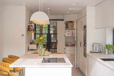 This is an example of a large contemporary grey and white single-wall open plan kitchen in London with flat-panel cabinets, white cabinets, black appliances, porcelain flooring, multiple islands, grey floors, white worktops and feature lighting.