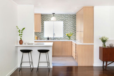 Inspiration for a mid-sized contemporary galley kitchen in Santa Barbara with a single-bowl sink, flat-panel cabinets, light wood cabinets, quartz benchtops, green splashback, ceramic splashback, stainless steel appliances, porcelain floors, a peninsula, grey floor and white benchtop.