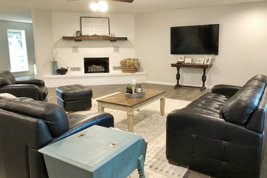Example of a large country open concept medium tone wood floor and brown floor living room design in Other with white walls, a standard fireplace, a brick fireplace and a wall-mounted tv
