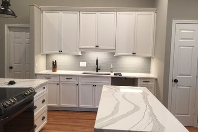 Example of a mid-sized trendy light wood floor eat-in kitchen design in Other with a single-bowl sink, shaker cabinets, white cabinets, quartz countertops, gray backsplash, glass tile backsplash, stainless steel appliances and an island