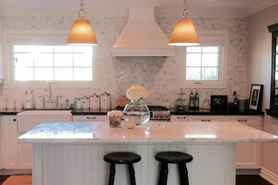 Mid-sized transitional l-shaped dark wood floor and brown floor eat-in kitchen photo in Toronto with an island, a farmhouse sink, recessed-panel cabinets, white cabinets, marble countertops, gray backsplash, matchstick tile backsplash and stainless steel appliances