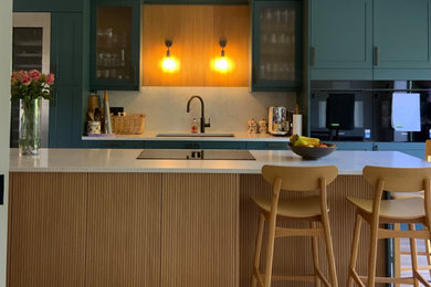 Photo of a large modern open plan kitchen in Buckinghamshire with shaker cabinets, quartz worktops, white splashback, engineered quartz splashback, vinyl flooring, an island, brown floors, white worktops, an integrated sink, green cabinets, integrated appliances and feature lighting.