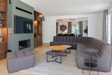 Aménagement d'un salon ouvert avec un mur vert, parquet clair, un poêle à bois, un manteau de cheminée en plâtre et un téléviseur encastré.